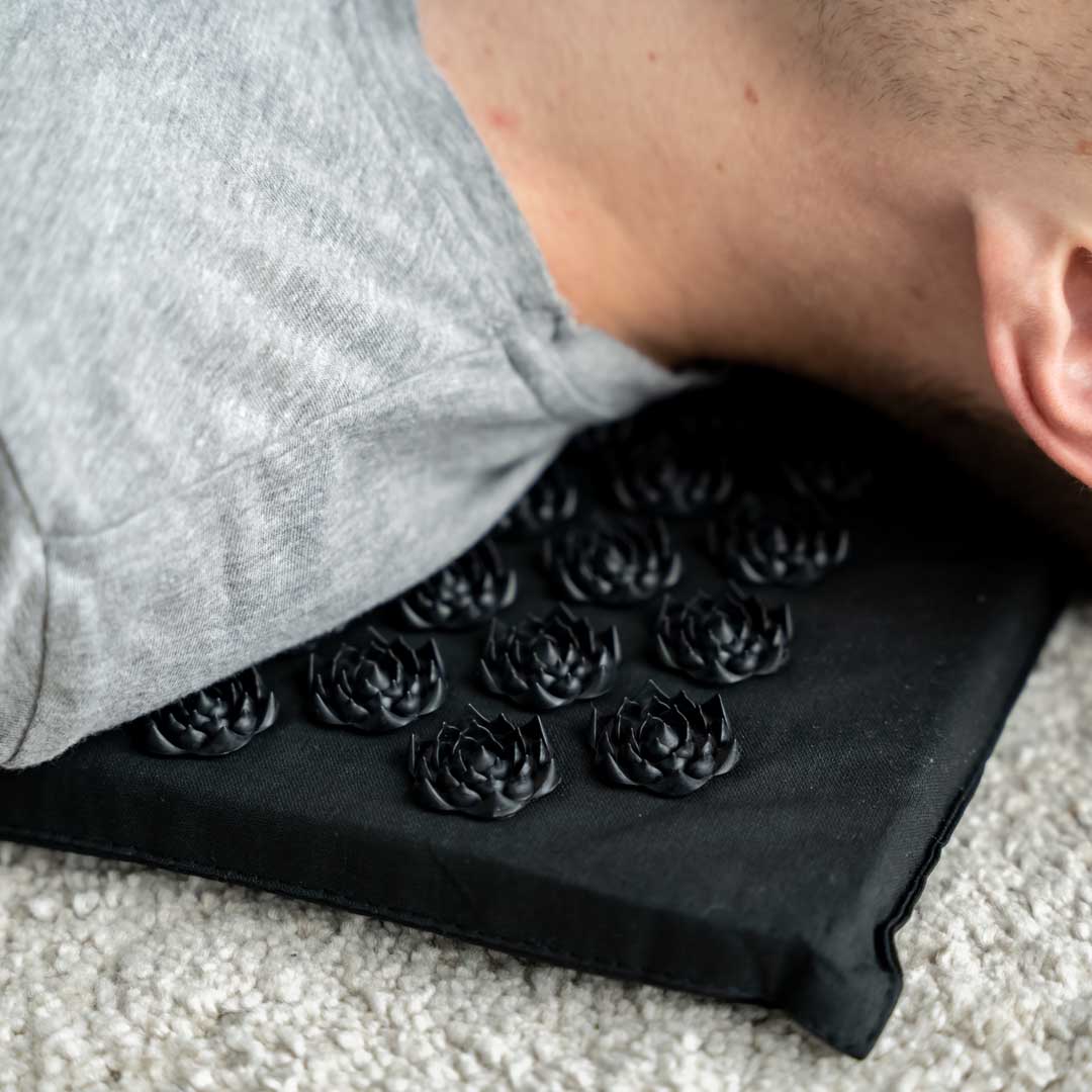 mand ligger på sort akupressurmåtte med pude acumat