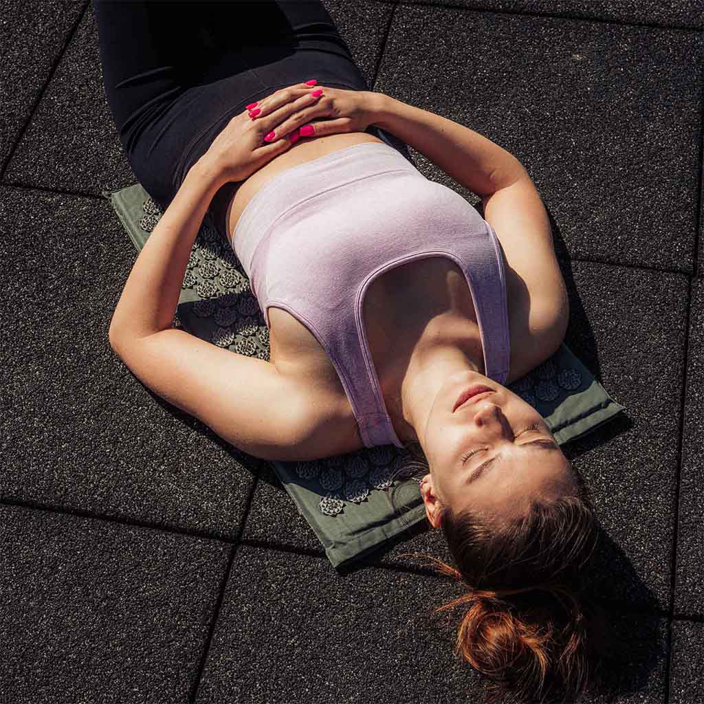 smuk kvinde liggende udenfor på sort akupressurmåtte acumat med pude
